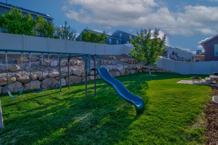 Expansive backyard featuring a green lawn, rock retaining wall, and a vinyl privacy fence