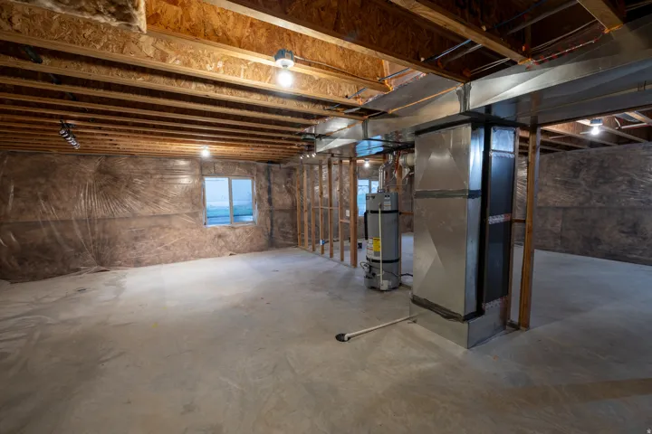 Unfinished basement with exposed ceiling joists, concrete flooring, and a single window