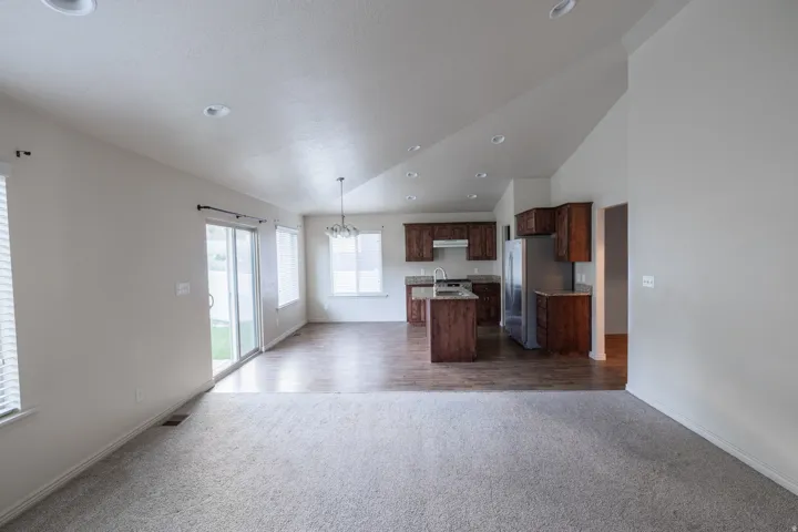 Vaulted ceiling with recessed lighting, wood-finish flooring, kitchen island, stainless steel refrigerator, and ample natural light