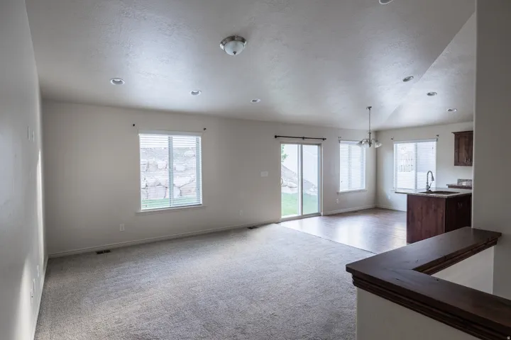 Open-concept living area featuring recessed lighting, a vaulted ceiling, wood-finish flooring, a sliding glass door, and a built-in kitchen island with a sink