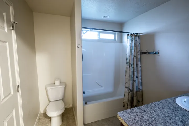 Bathroom featuring a white toilet, white tub-shower combination, high window, and a countertop with an integrated sink