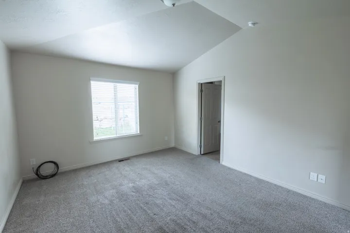 Vaulted ceilings, neutral wall tones, window with horizontal blinds, gray carpeting, and a white interior door
