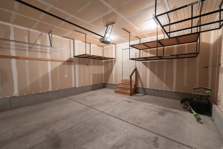 Concrete flooring, multiple overhead storage racks, built-in wooden shelving, rear access door, wood stairwell