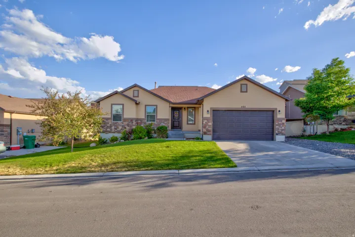Single-story residence featuring a two-car garage, stone facade accents, and a front yard with mature landscaping