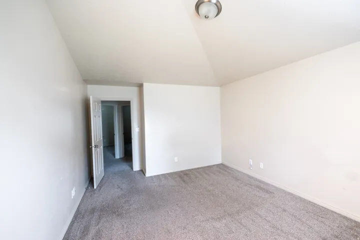 Vaulted ceiling, neutral wall tones, gray carpeting, and brushed nickel flush-mount lighting