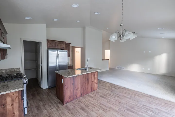Kitchen featuring wood-finish flooring, granite countertops, stainless steel appliances, and a central island with an integrated sink