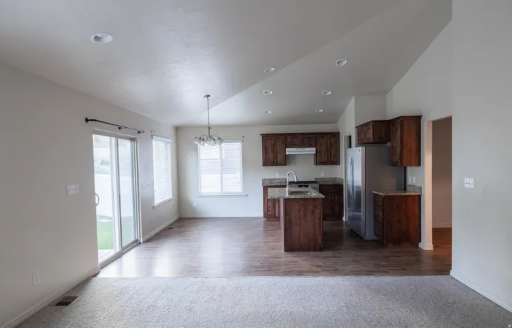 Vaulted ceiling with recessed lighting, wood-finish flooring, sliding glass patio door, kitchen with wood cabinetry, and stainless steel appliances