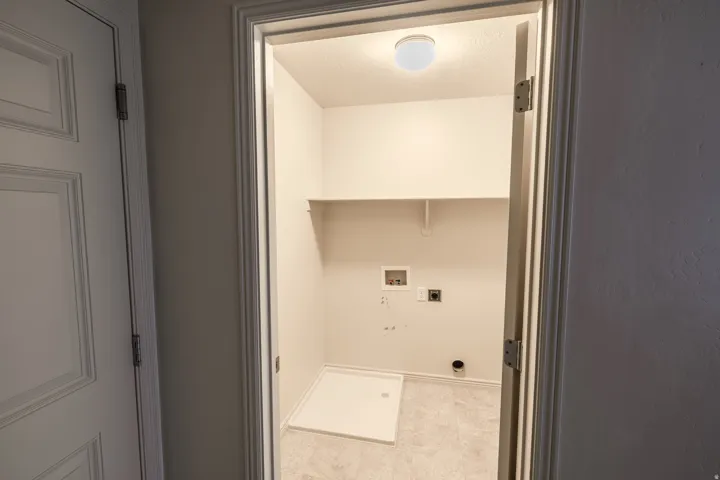 Dedicated utility closet featuring a built-in shelf, overhead lighting, and utility hookups
