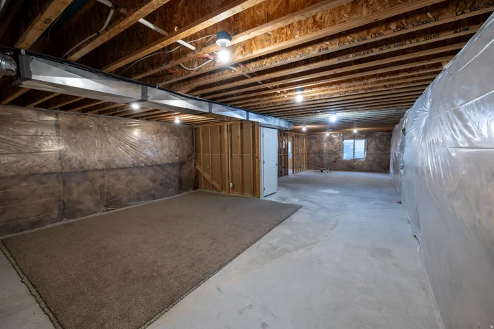 Unfinished basement with exposed ceiling joists, concrete flooring, recessed lighting, and framed interior walls
