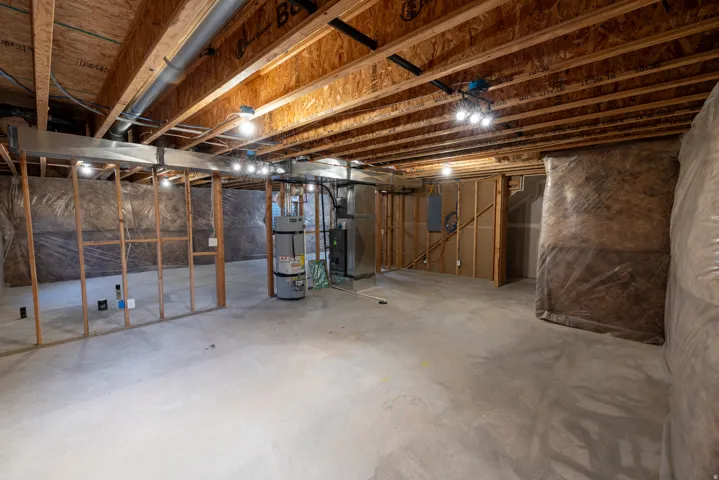 Unfinished basement with concrete flooring, exposed wood joists, and utility access