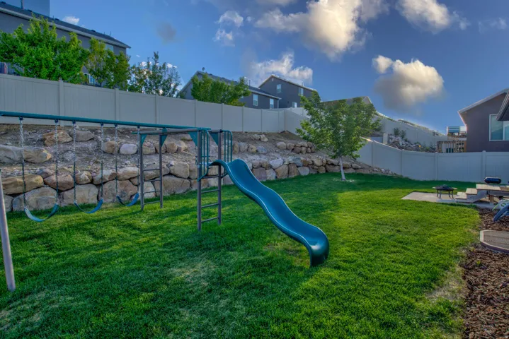 Expansive yard featuring a green lawn, rock retaining wall, and privacy fencing