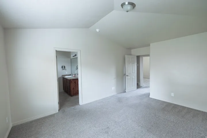 Vaulted ceiling with flush-mount lighting, light gray carpet, white painted walls, and a visible bathroom vanity with a single sink