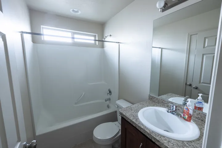 Bathroom featuring a single vanity with a granite-look countertop, an integrated sink, a large wall-mounted mirror, a tub/shower combination, and a horizontal window