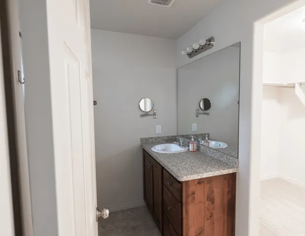 Dual vanity with integrated sinks, speckled countertop, wood-finish cabinetry, full-width mirror, and overhead vanity lighting