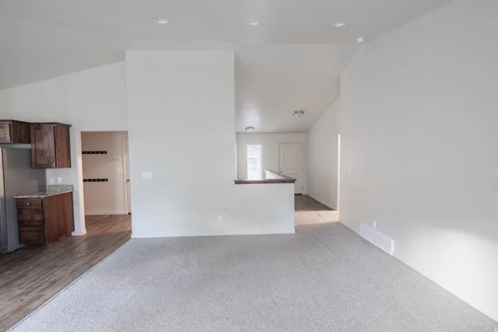 Vaulted ceilings with recessed lighting, wood-finish flooring, and a kitchen featuring dark wood cabinetry and stone countertops