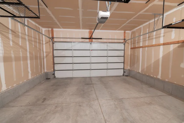 Overhead garage door with automatic opener, concrete flooring, and built-in overhead storage racks