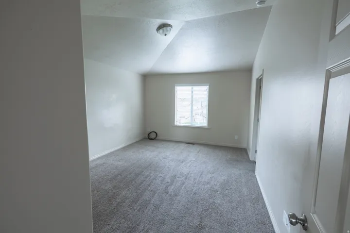 Spacious room with gray textured carpeting, a single window with horizontal blinds, and a flush-mount ceiling light fixture