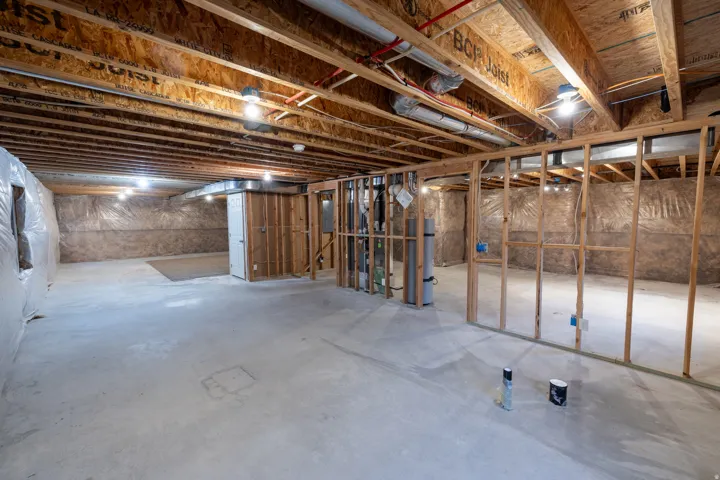 Unfinished basement featuring exposed wood joists, framed wall partitions, and a concrete floor