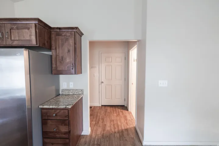 Stainless steel refrigerator, wood-finish cabinetry, granite-style countertop, and wood-finish flooring