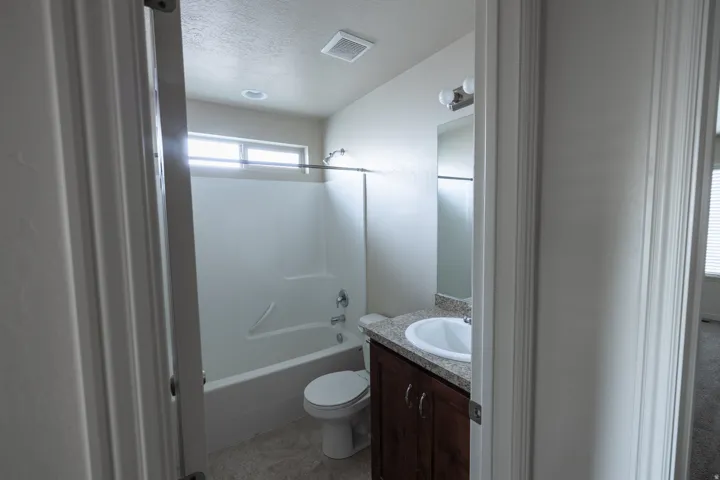 Bathroom featuring a single vanity with dark wood-finish cabinetry, a white basin sink, a wall-mounted mirror, and a shower-tub combination with a window