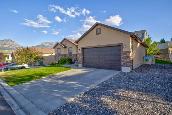 Stucco and stone exterior featuring an attached two-car garage, a concrete driveway, and a gravel parking area