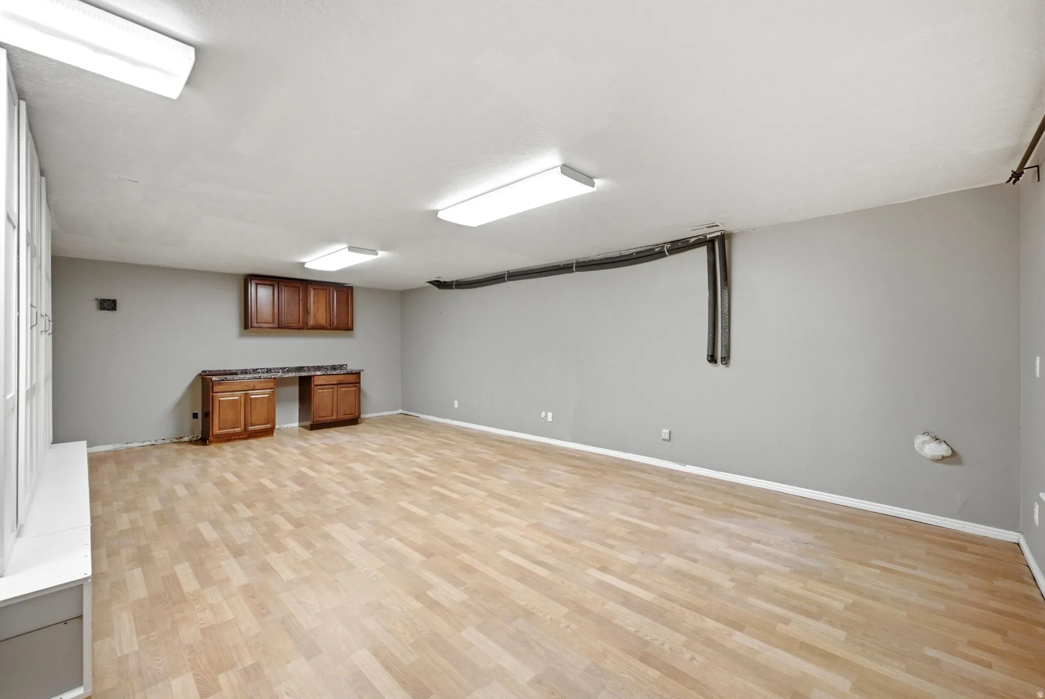 Main home basement. Spacious room featuring wood-finish flooring, neutral gray walls, and bright overhead lighting