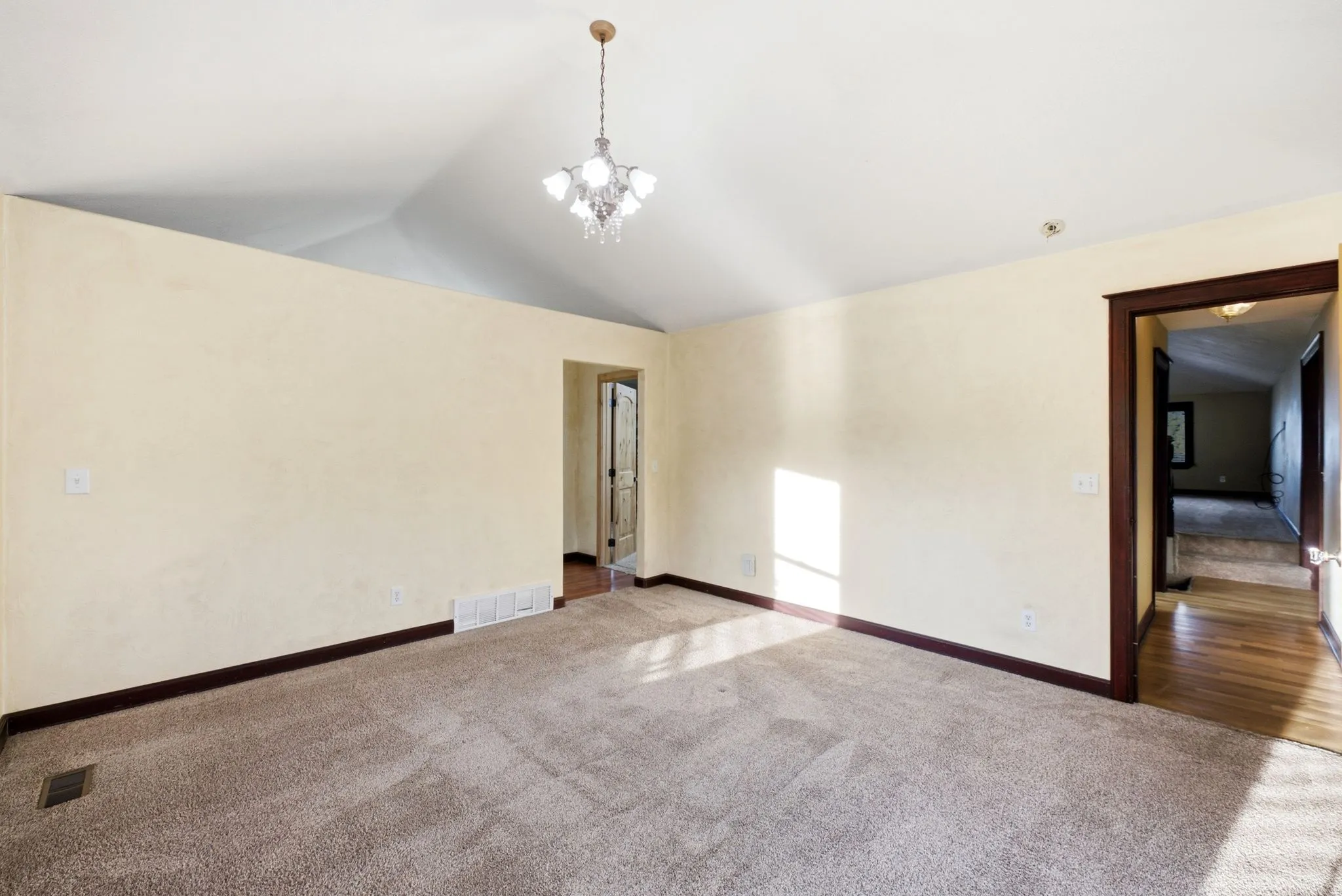 Master suite, vaulted ceiling with a chandelier, carpet flooring, and dark wood trim