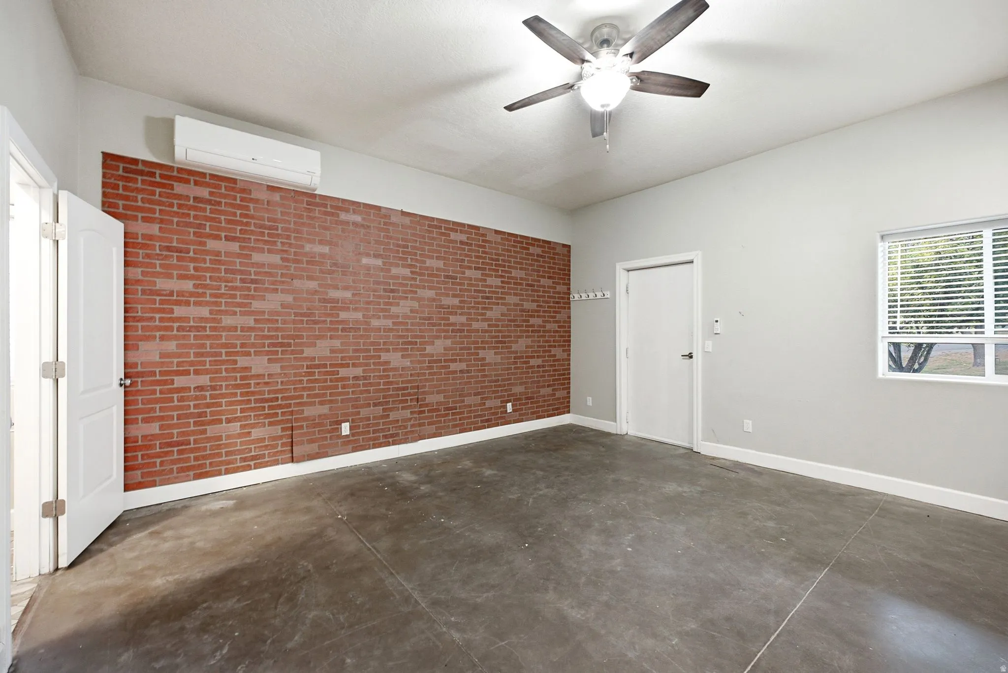 Spacious room featuring an exposed brick accent wall and concrete flooring