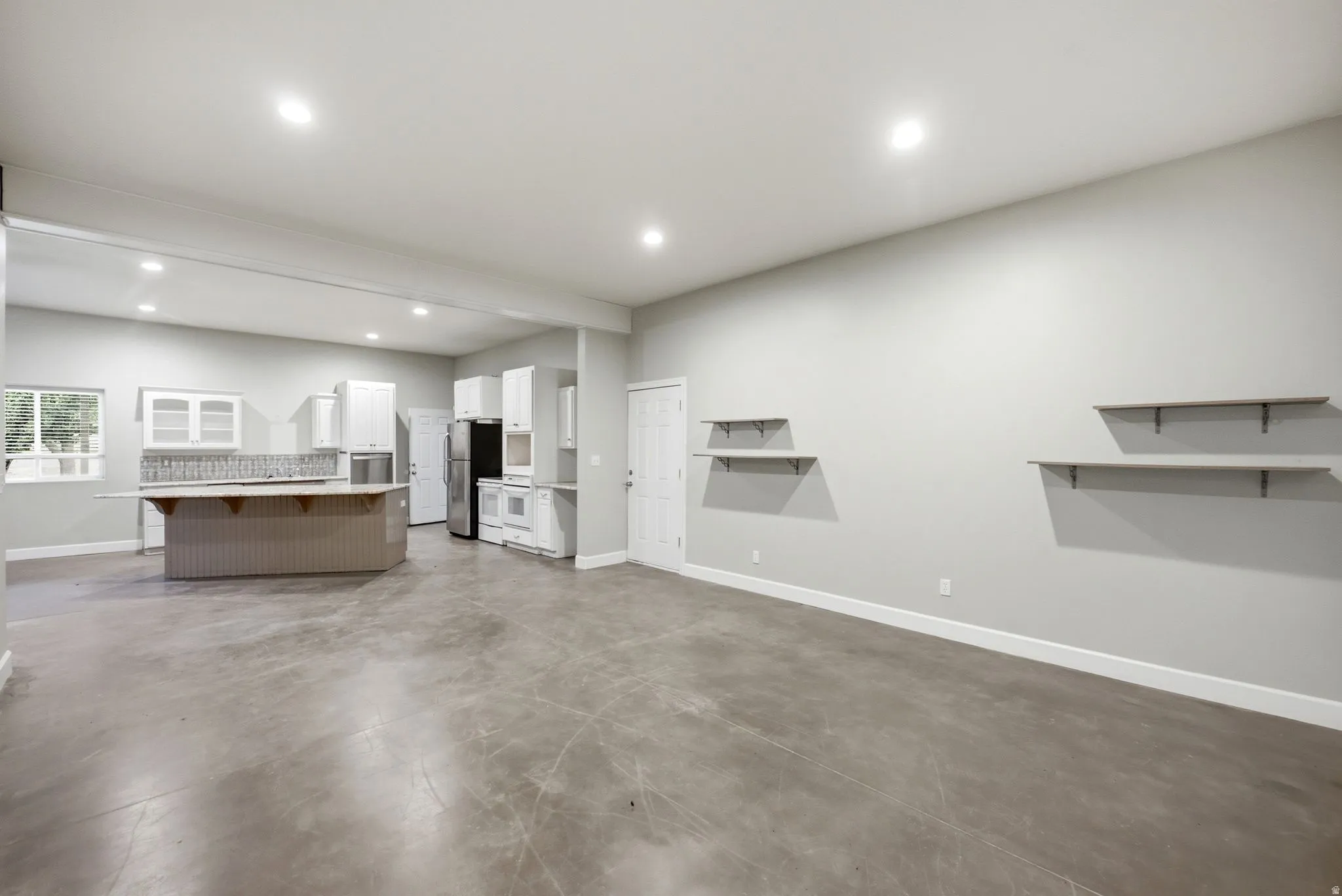 Apartment in the shop. Open concept living area featuring a kitchen with white cabinetry, a central island with counter seating, a tiled backsplash, and recessed lighting