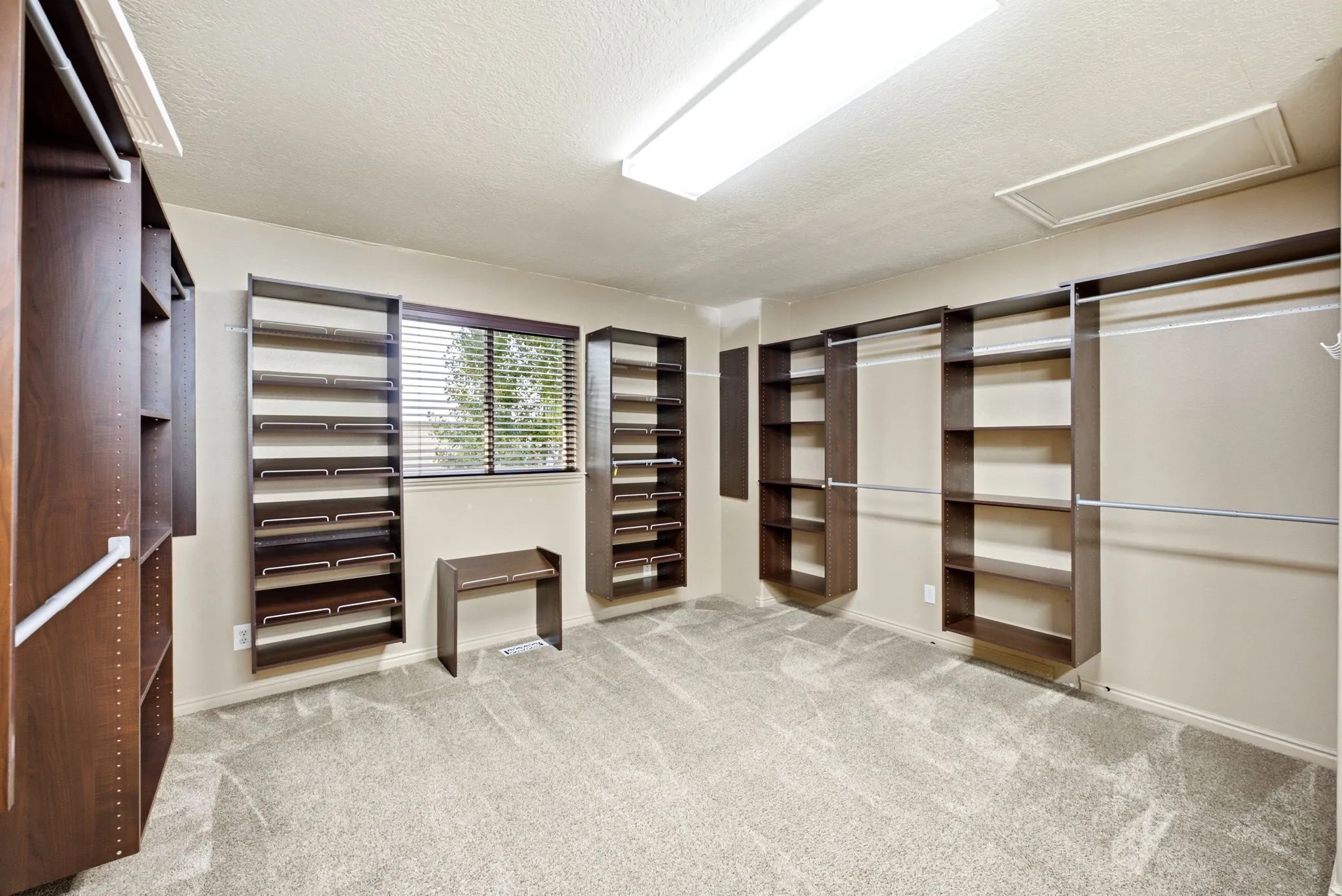 Master walk-in closet. Spacious walk-in closet featuring extensive built-in shelving, hanging rods, light-toned walls, gray carpet, and a window with blinds