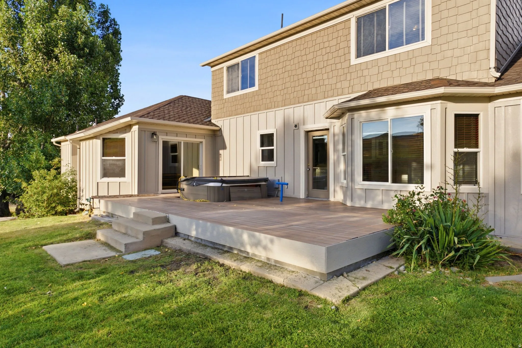 Expansive rear deck featuring wood-finish composite decking, concrete steps, and direct access to the interior via a sliding glass door and a glass-paneled door