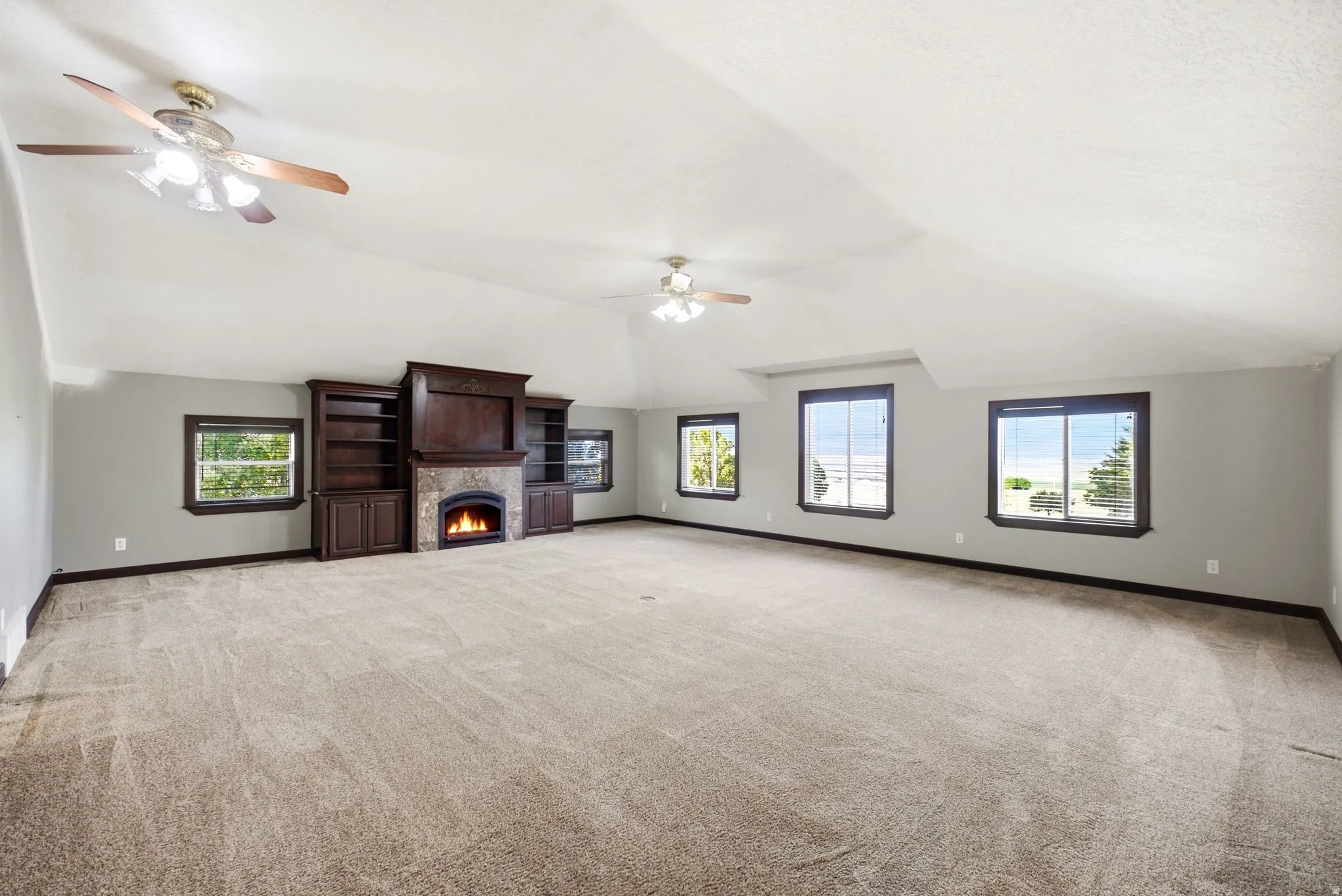 Spacious room featuring vaulted ceilings, a built-in entertainment center with stone surround fireplace, multiple windows, and two ceiling fans