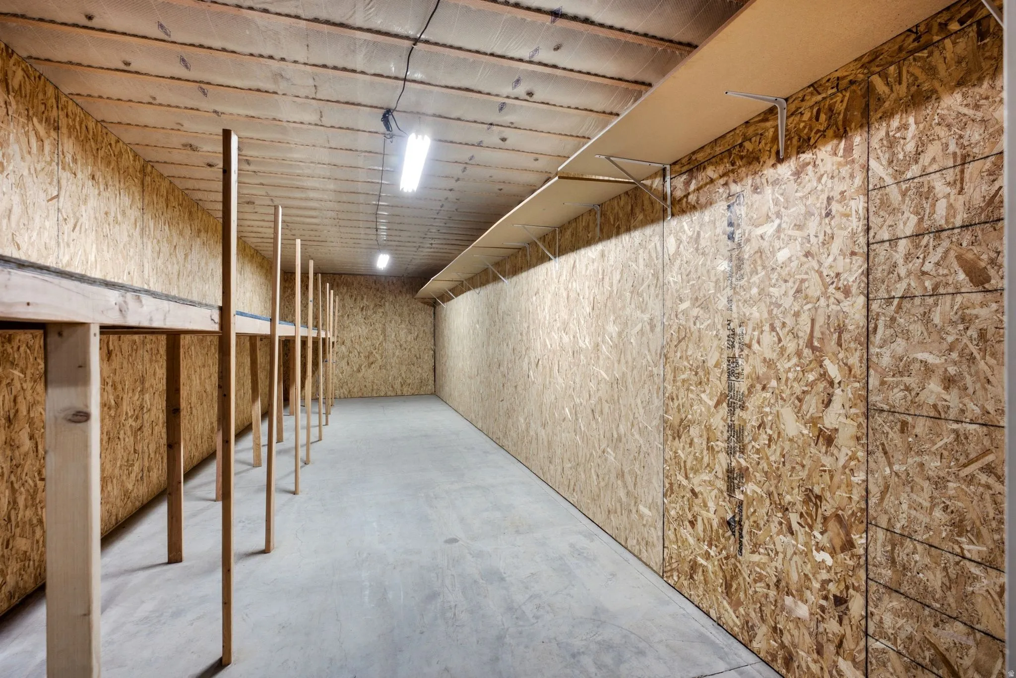Spacious storage area featuring concrete flooring, wood-finish paneling, built-in shelving, and overhead fluorescent lighting