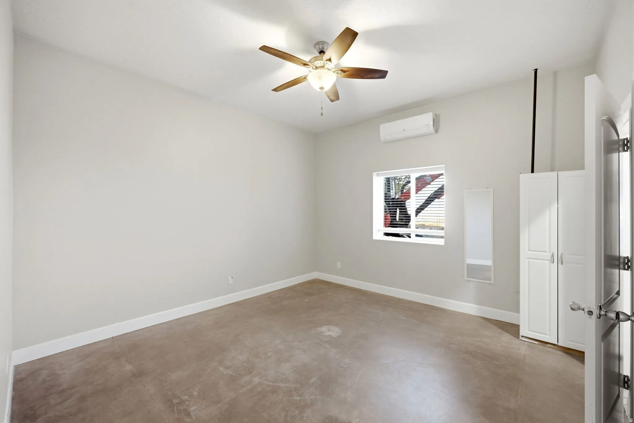 Apartment in the shop. Bedroom featuring light-colored walls, wood-finish ceiling fan, concrete flooring, and a window with horizontal blinds