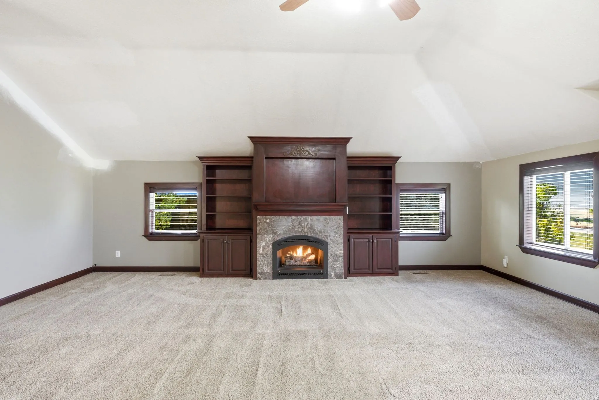 Spacious room featuring vaulted ceilings, light-toned carpet flooring, and a central fireplace with stone surround and built-in cabinetry