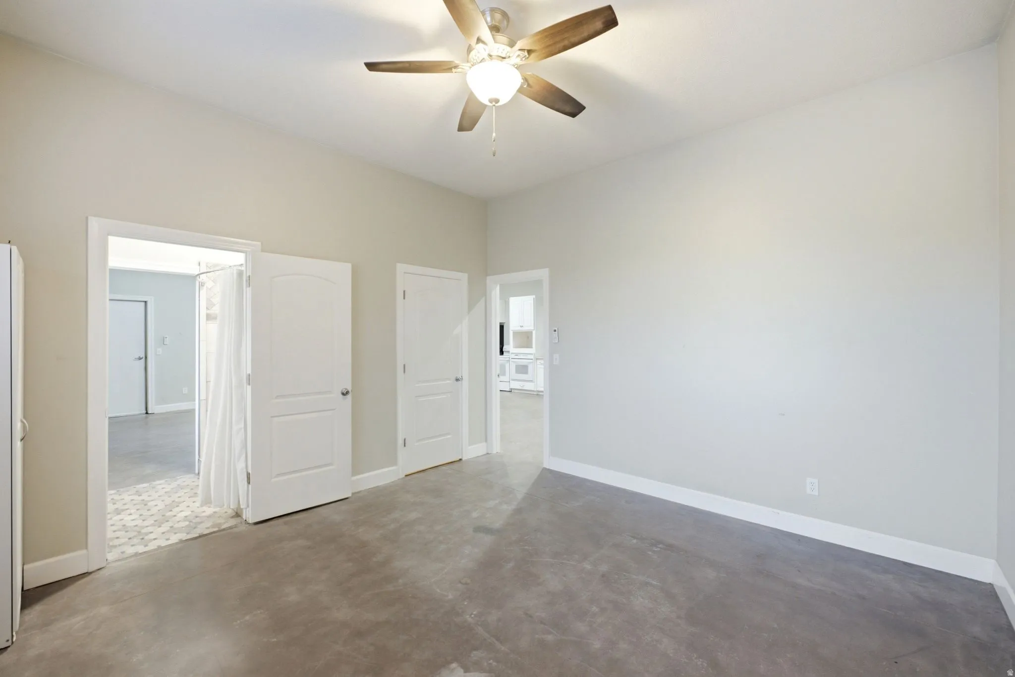 Apartment in the shop. Spacious room featuring light gray walls, a ceiling fan with wooden blades, and concrete flooring