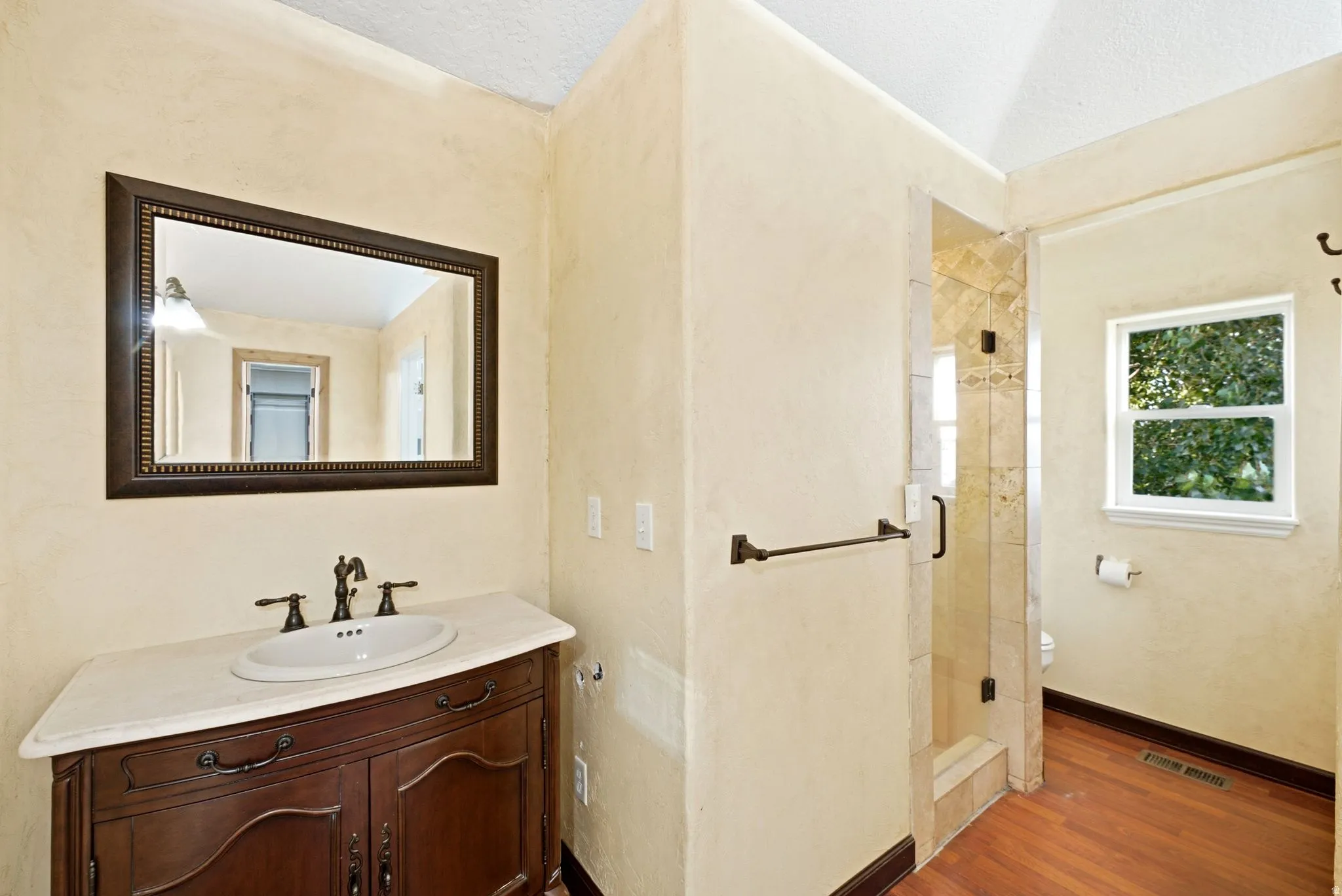 Master Bathroom featuring a wood-finish vanity with a single basin sink and bronze-finish faucet, framed mirror, and a tiled shower enclosure with a clear glass door