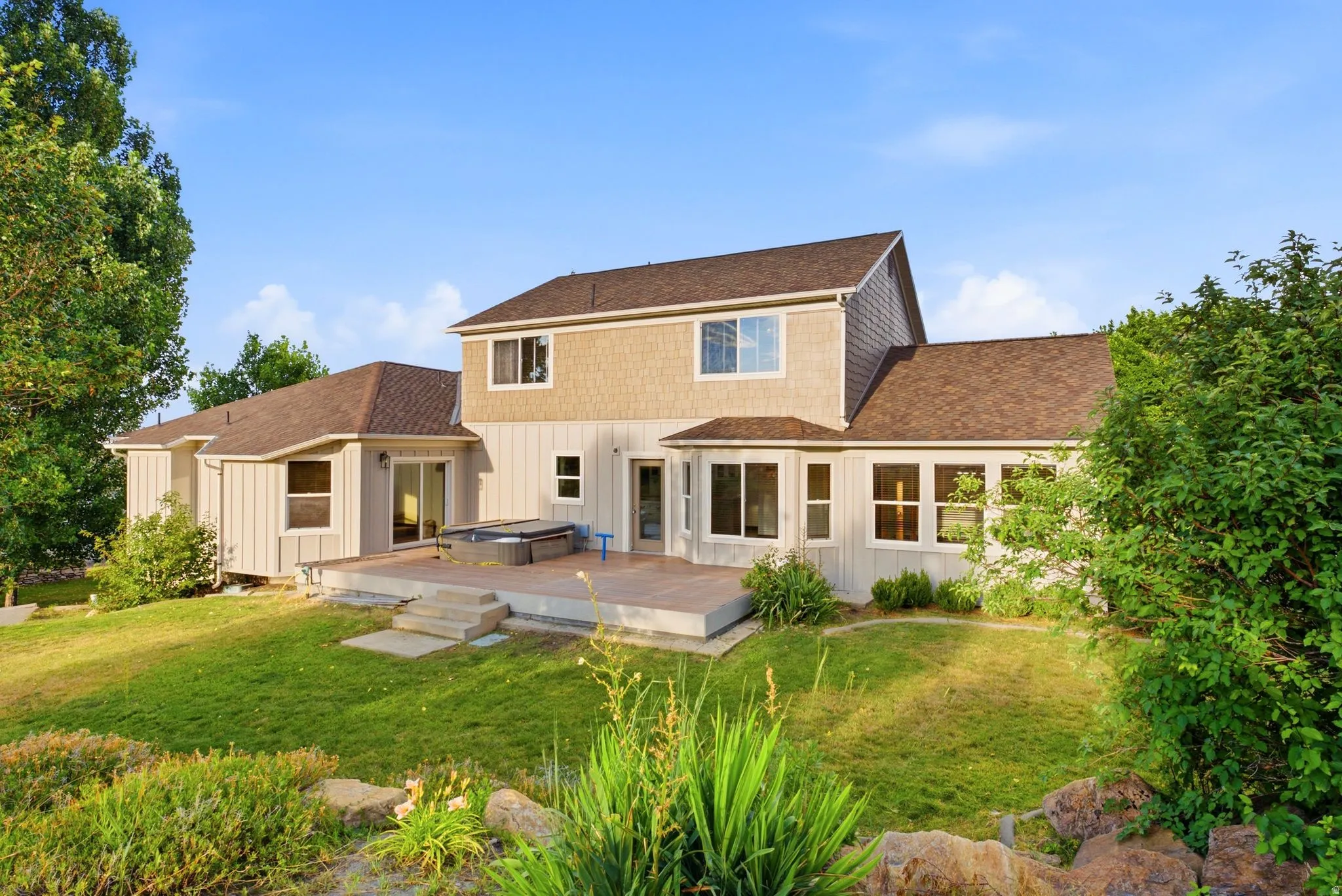 Rear exterior featuring a multi-level deck, board and batten siding, shake siding accents, multiple large windows, and a sloped lawn with mature landscaping