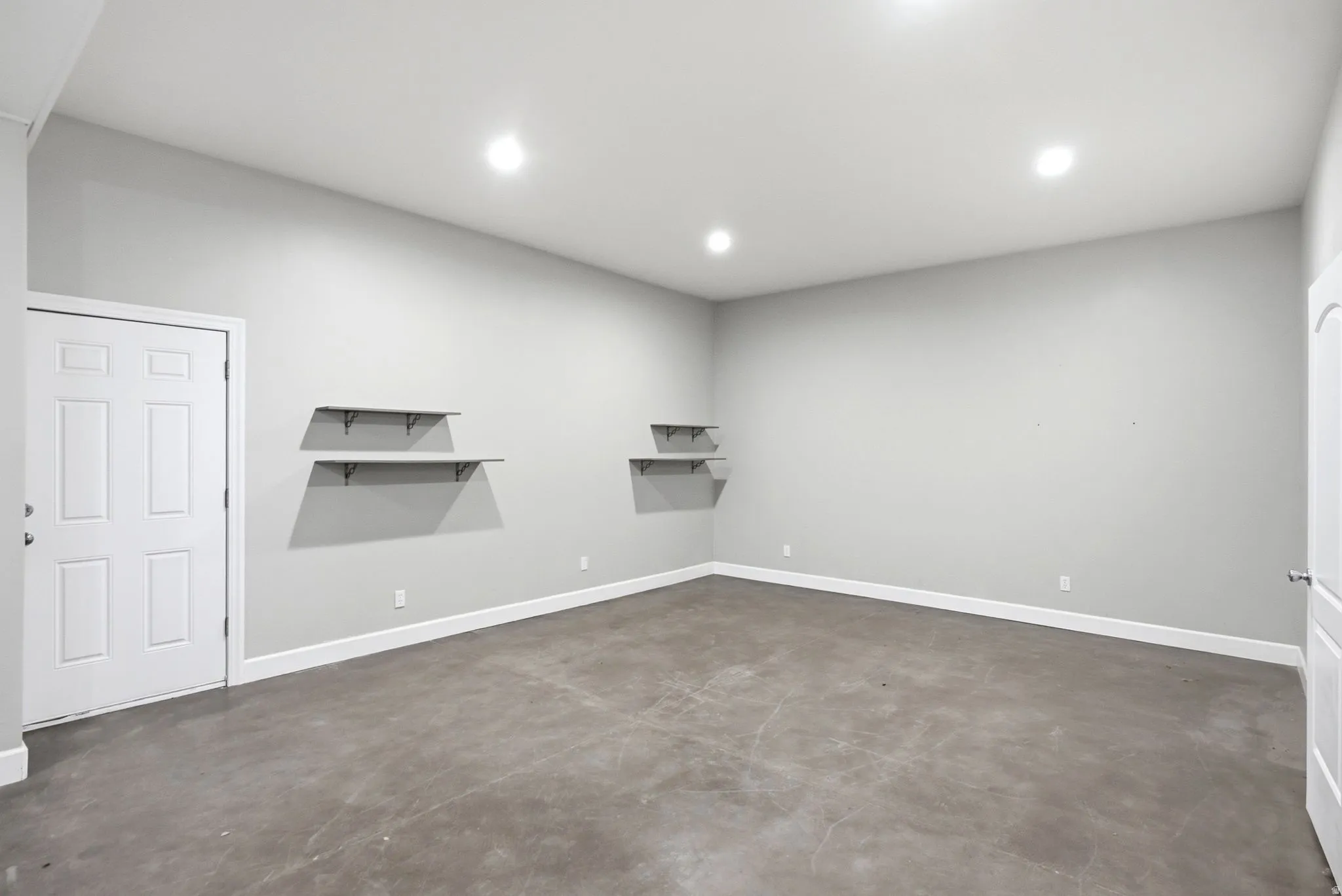 Apartment in the shop. Spacious room with concrete flooring, recessed lighting, white baseboards, and built-in wall shelving
