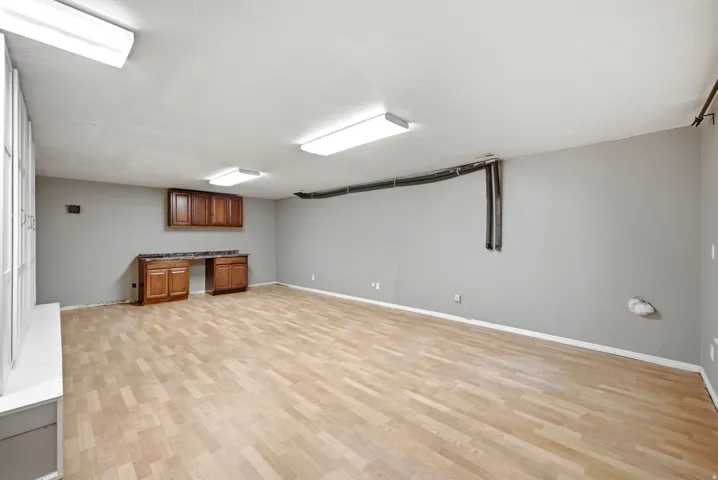 Main home basement. Spacious room featuring wood-finish flooring, neutral gray walls, and bright overhead lighting