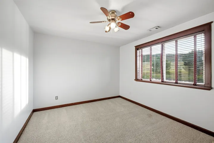 Upstairs bedroom. Carpeted room featuring a ceiling fan with integrated lighting, a large window with wood-finish trim, and horizontal blinds