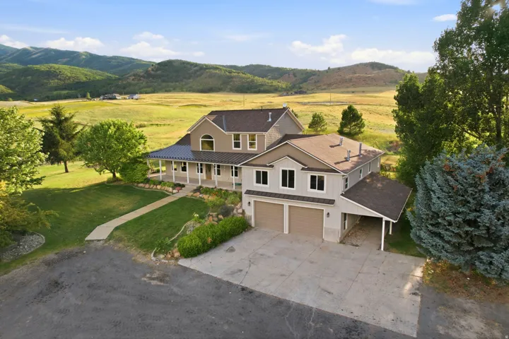 Two-story residence featuring a covered front porch, dual garage doors, a covered carport, and a surrounding green landscape
