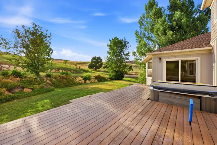 Expansive wood-finish deck featuring a built-in hot tub, providing direct access to the interior via a sliding glass door