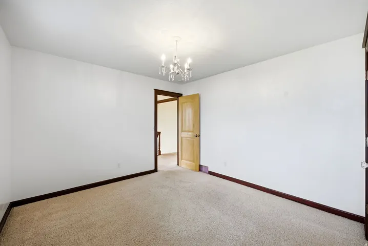 Main home upstairs. Neutral carpeted room featuring a chandelier, white walls, and dark wood trim