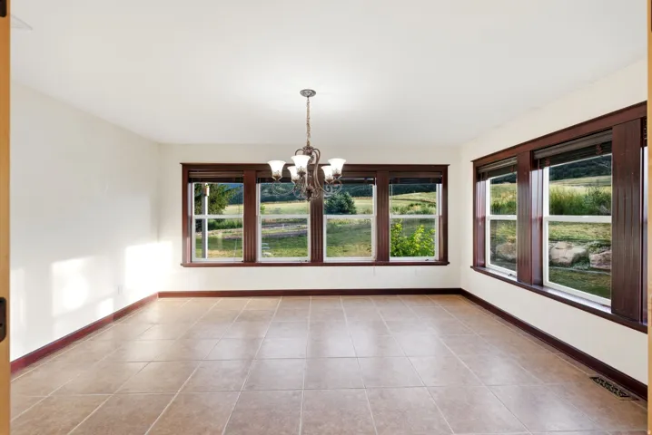 Formal dinning area. Expansive room featuring multiple windows with dark wood trim, a central chandelier, and neutral-toned tile flooring