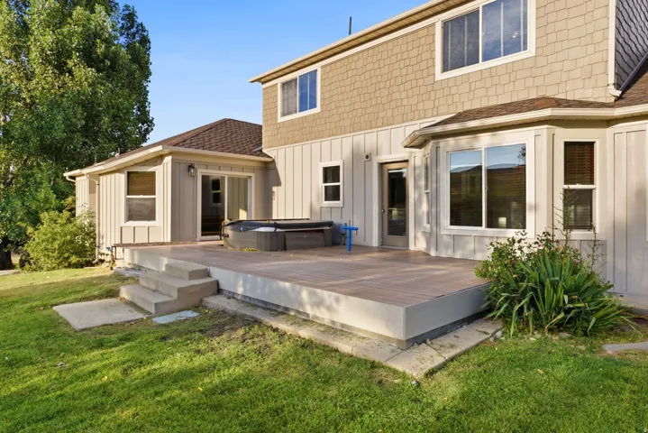 Expansive rear deck featuring wood-finish composite decking, concrete steps, and direct access to the interior via a sliding glass door and a glass-paneled door