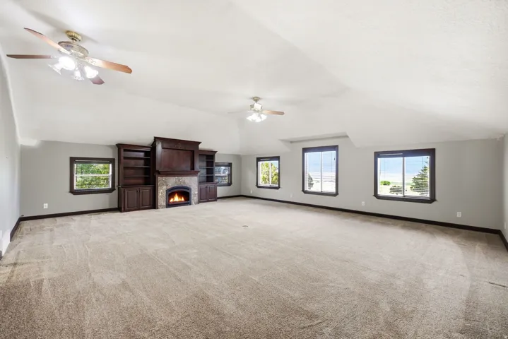 Spacious room featuring vaulted ceilings, a built-in entertainment center with stone surround fireplace, multiple windows, and two ceiling fans