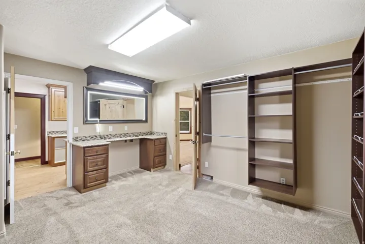 Master walk-in closet. Built-in vanity with an illuminated mirror, granite-look countertop, and custom cabinetry