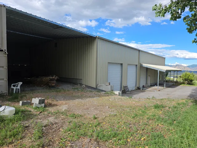 Large industrial building with corrugated metal siding, featuring two roll-up doors, an attached covered awning, and an expansive open-sided storage area
