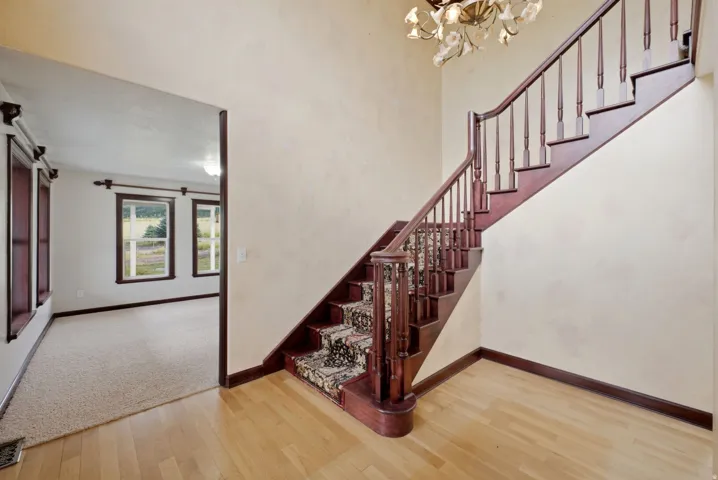 Foyer featuring wood-finish flooring, a grand staircase with carved wood banister, decorative newel post, and patterned stair runner